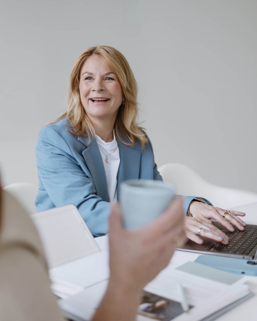 Frau lächelnd eine andere Person an während sie am Laptop tippt