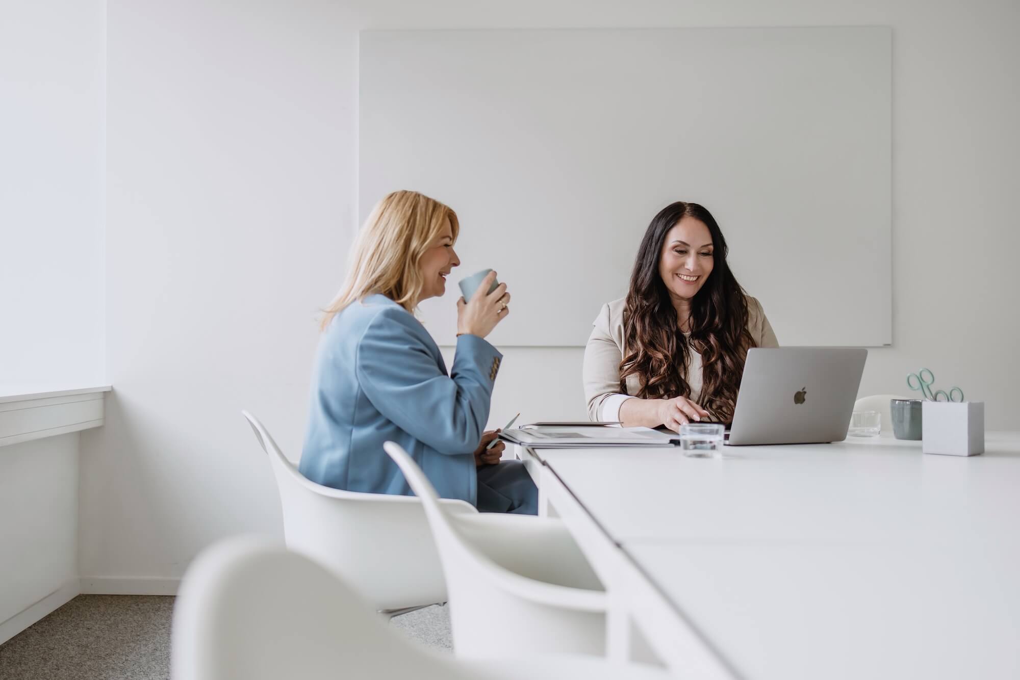Zwei Frauen sitzen mit einem Laptop am Meetingtisch und unterhalten sich
