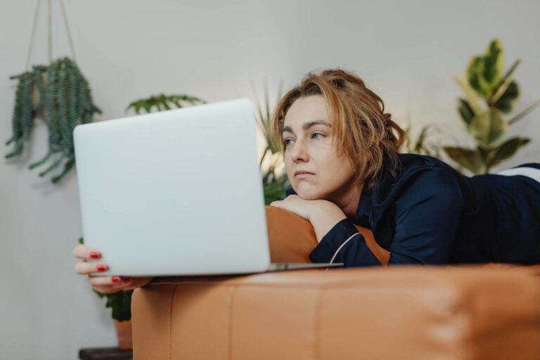 Frau liegt auf dem Sofa und schaut traurig auf ihren Laptop